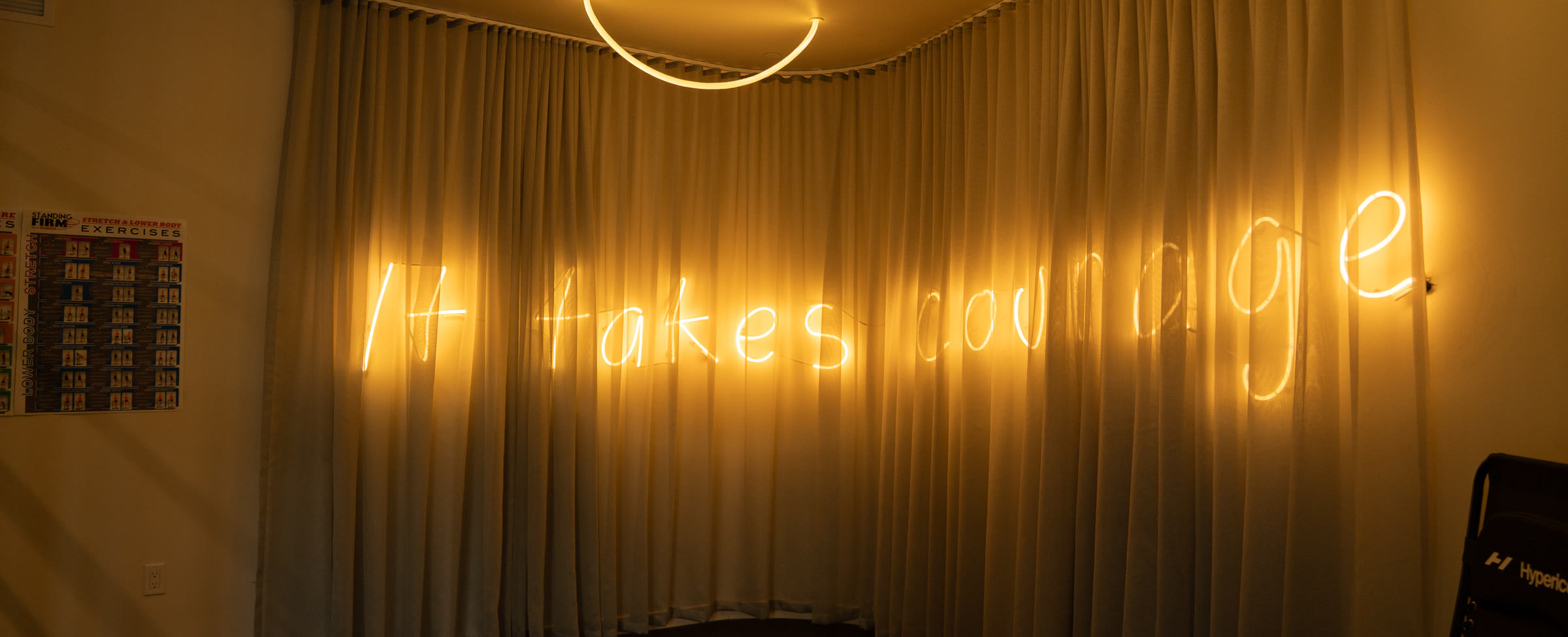 Curtained recovery room lit by a neon sign reading “It takes courage”