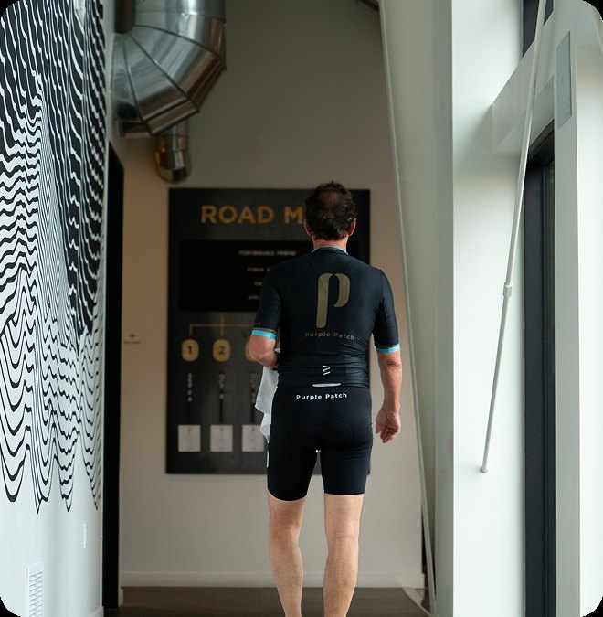 A cyclist in Purple Patch kit by the Road Map wall