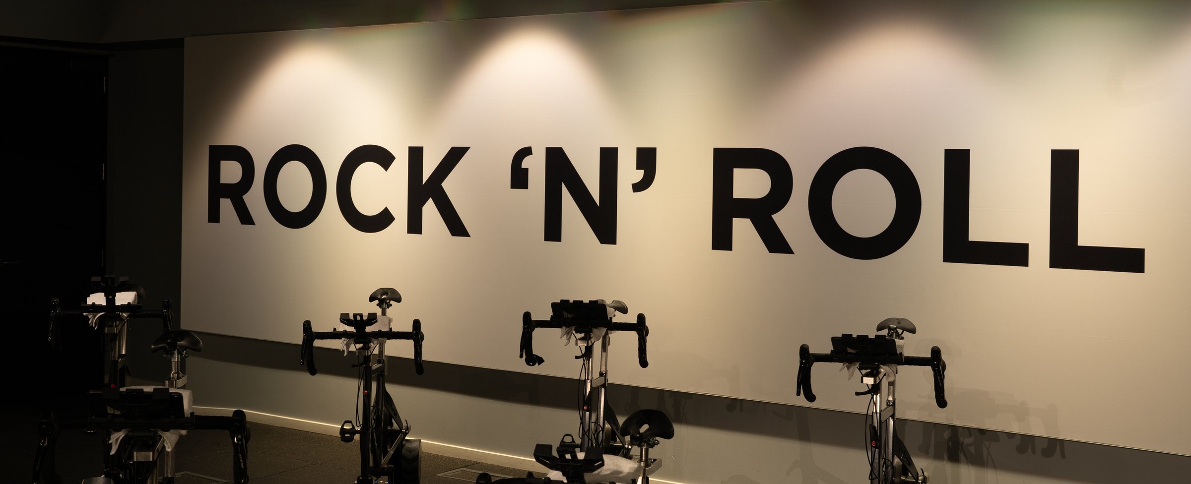 Bikes lined up in the cycling studio under the “Rock ’n’ Roll” wall